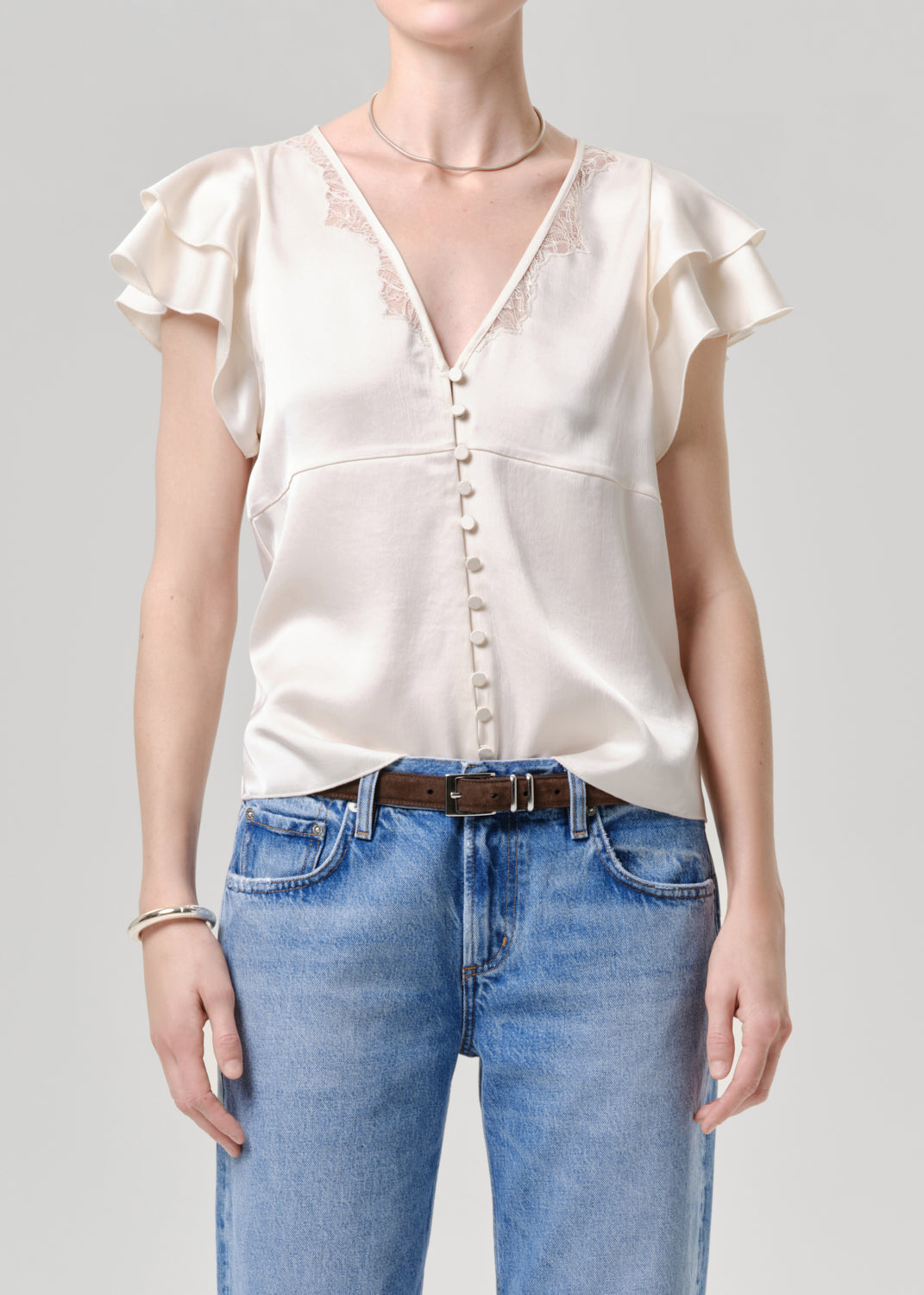 Person wearing a white blouse with ruffled sleeves and blue jeans on a grey background