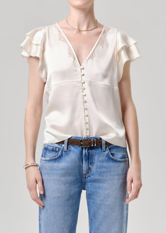 Person wearing a white blouse with ruffled sleeves and blue jeans on a grey background