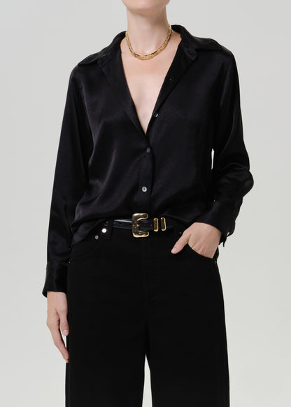Woman wearing a black satin button-up shirt with black wide leg pants on a grey background.