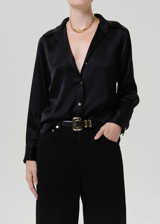 Woman wearing a black satin button-up shirt with black wide leg pants on a grey background.