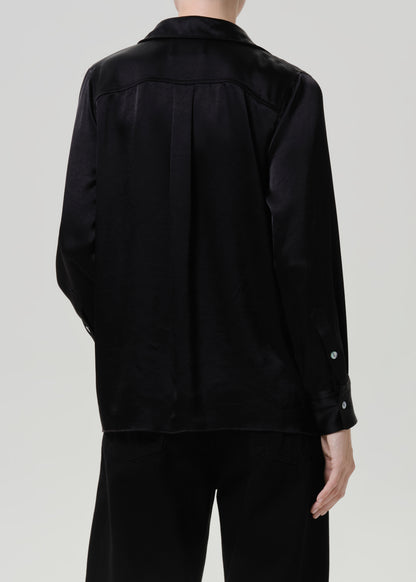 Woman wearing a black satin button-up shirt with black wide leg pants viewed from the back on a grey background.