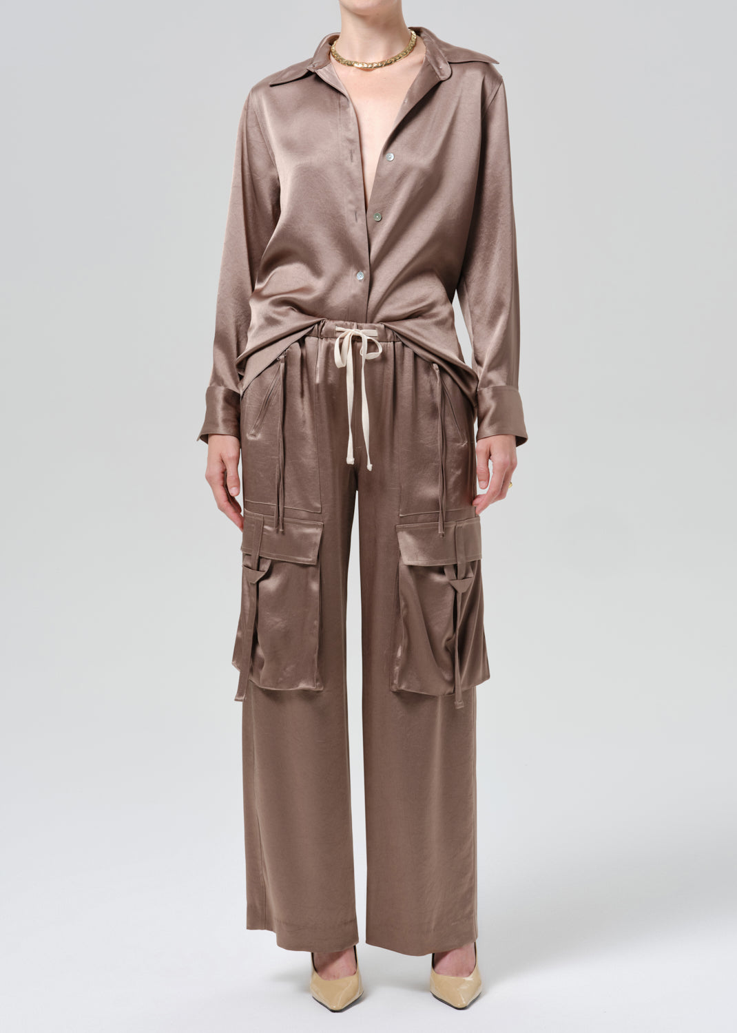 Person wearing a taupe satin button front blouse with taupe cargo pants on a grey background
