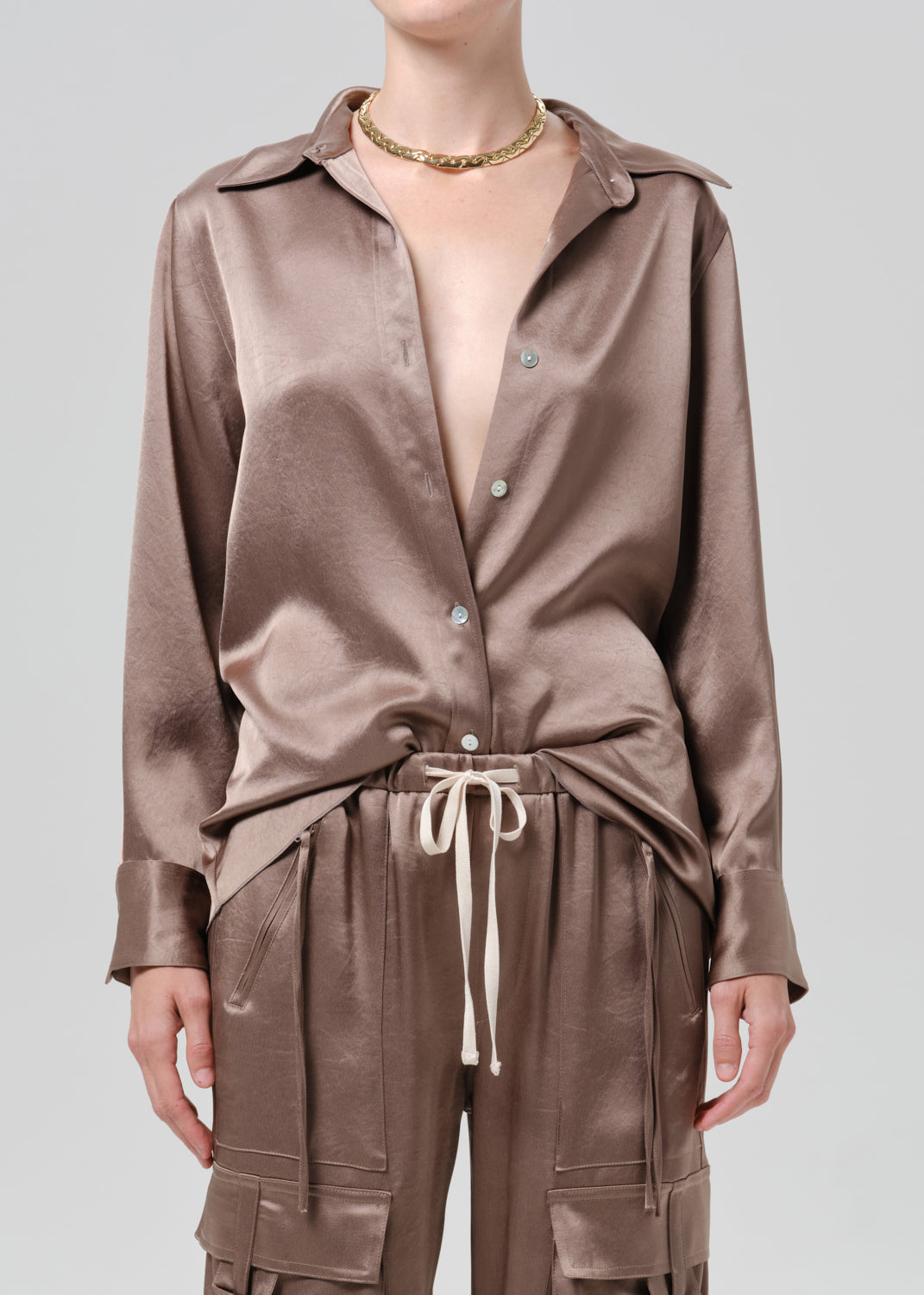 Person wearing a taupe satin button front blouse on a grey background