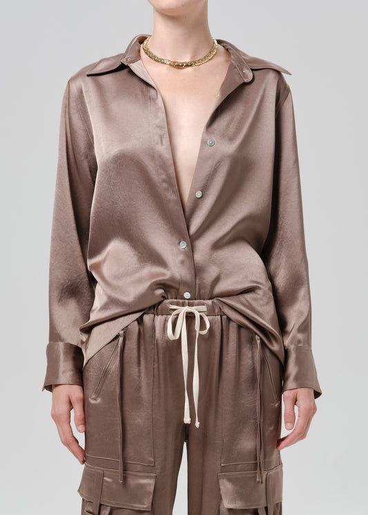 Person wearing a taupe satin button front blouse on a grey background