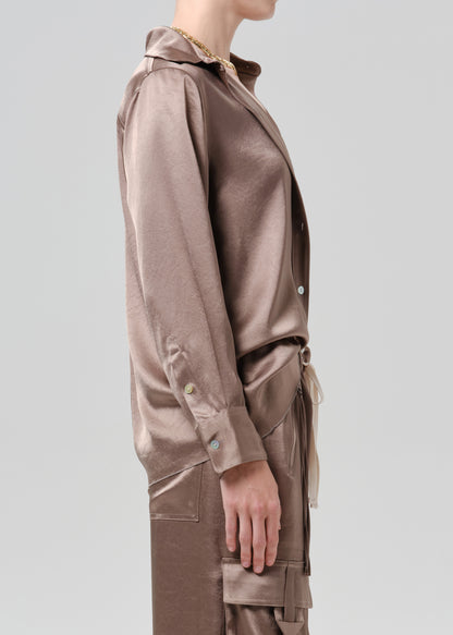 Person wearing a taupe satin button front blouse with taupe cargo pants viewed from the side on a grey background