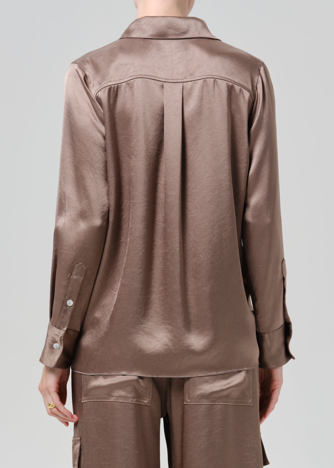 Person wearing a taupe satin button front blouse with taupe cargo pants viewed from the back on a grey background