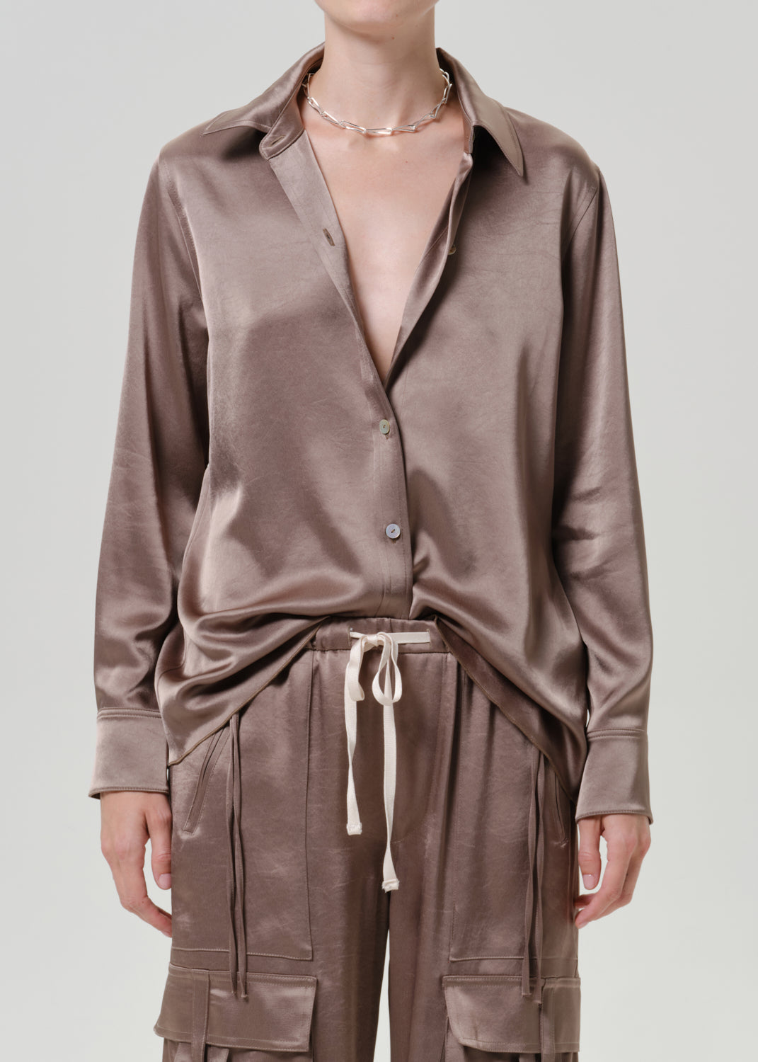 Woman wearing a taupe satin button-up shirt with matching taupe pants on a grey background.