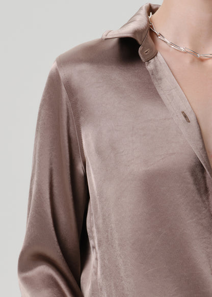 Close-up of a taupe satin button-up shirt on a grey background.