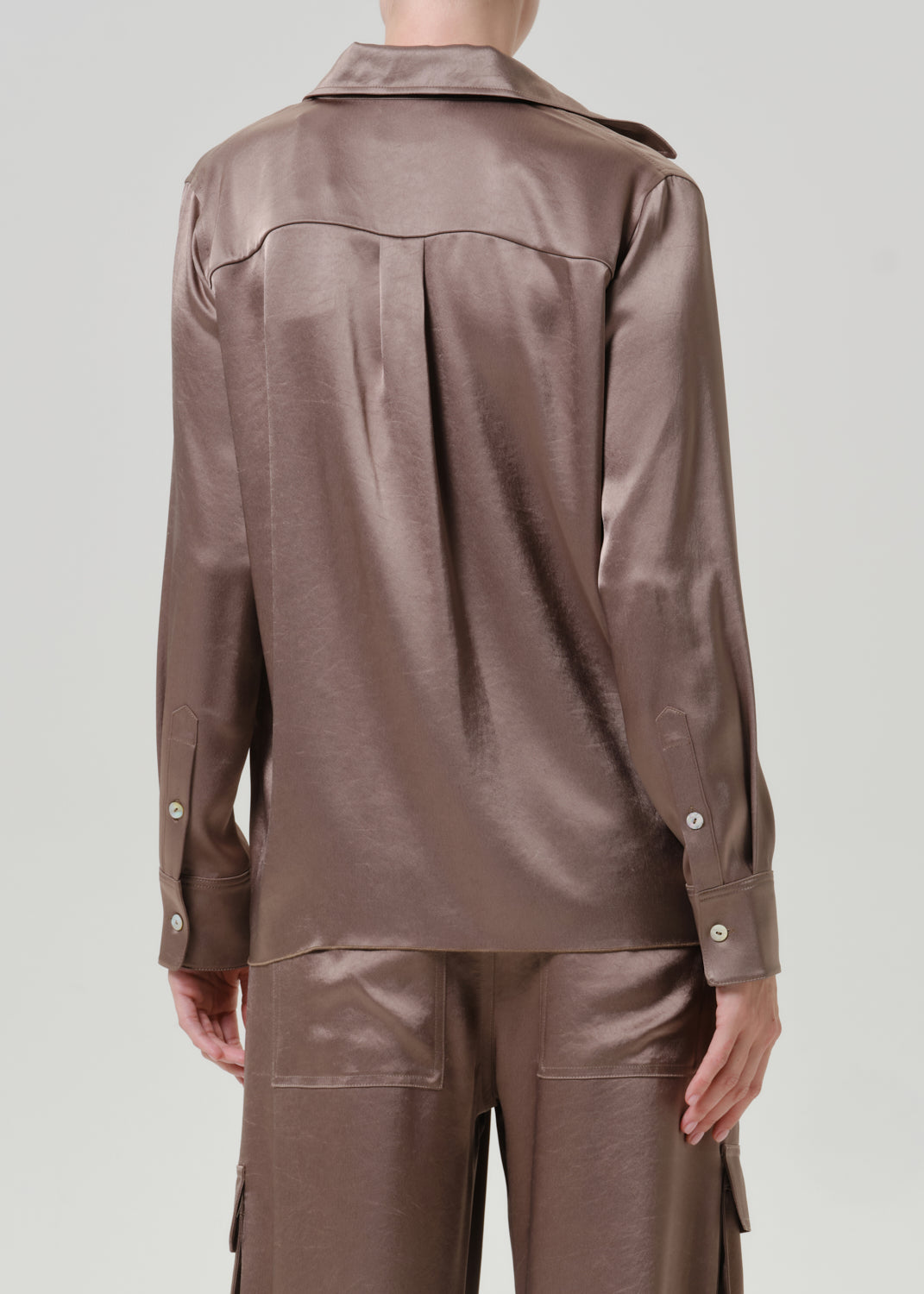 Woman wearing a taupe satin button-up shirt with matching taupe pants viewed from the back on a grey background.
