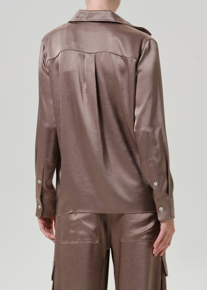 Woman wearing a taupe satin button-up shirt with matching taupe pants viewed from the back on a grey background.