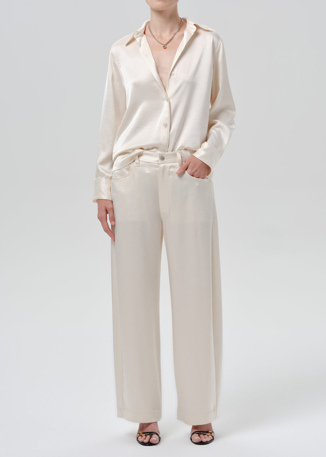Person wearing an ivory satin button front blouse with ivory wide leg trousers on a grey background