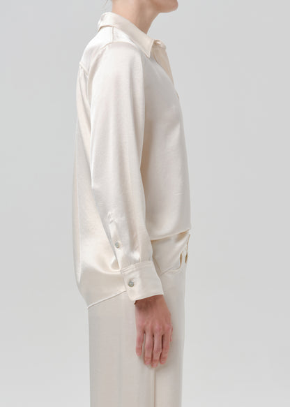 Person wearing an ivory satin button front blouse with ivory wide leg trousers viewed from the side on a grey background