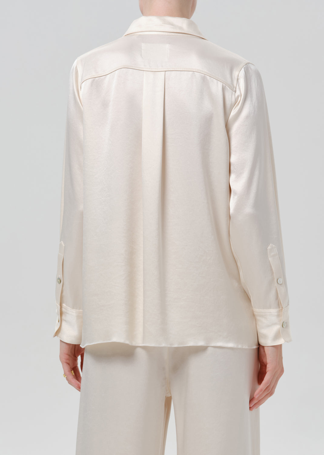 Person wearing an ivory satin button front blouse with ivory wide leg trousers viewed from the back on a grey background