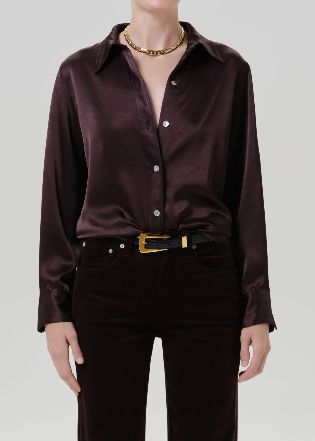 Person wearing a dark brown satin button front blouse on a grey background