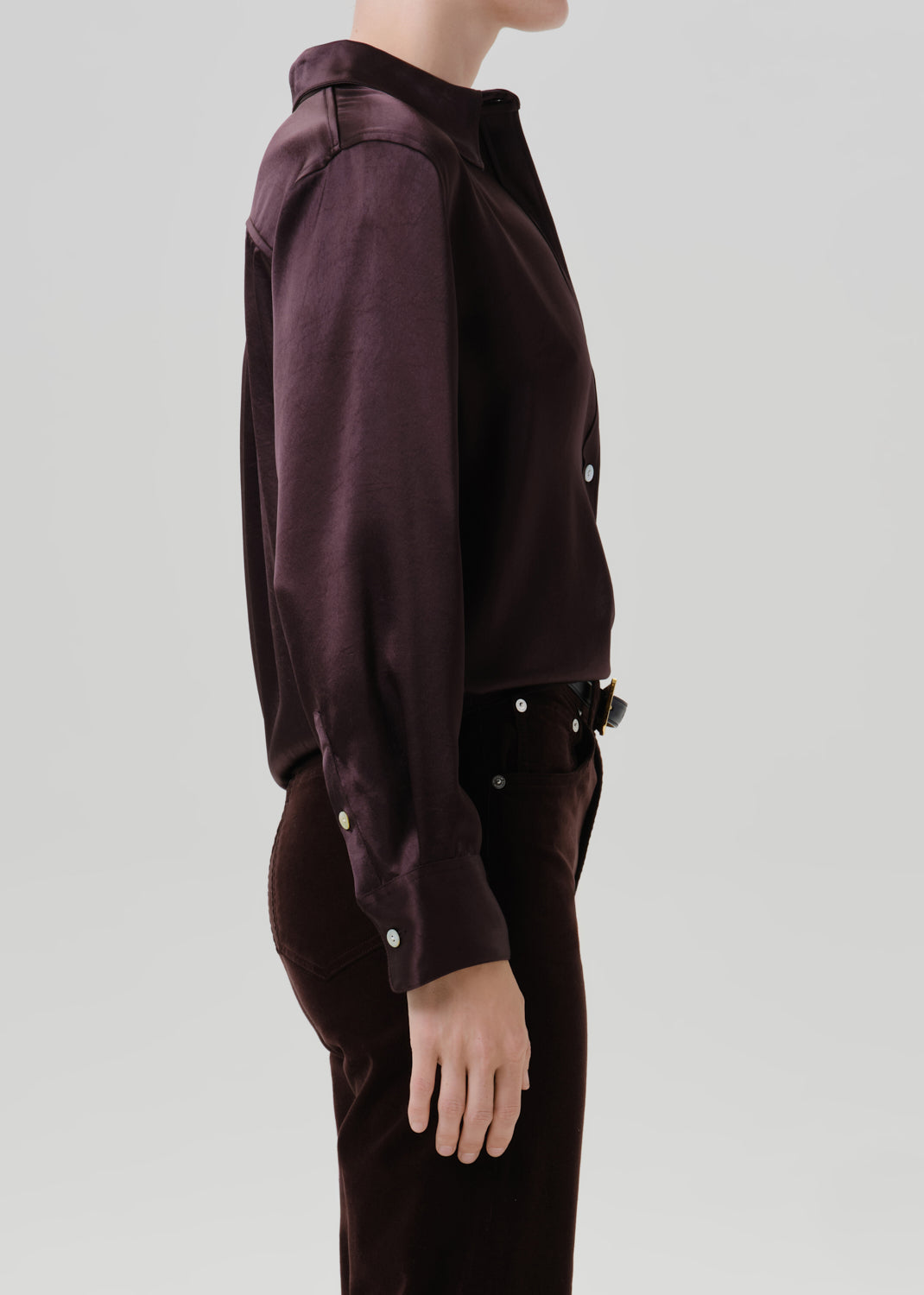 Person wearing a dark brown satin button front blouse with dark brown straight leg pants viewed from the side on a grey background
