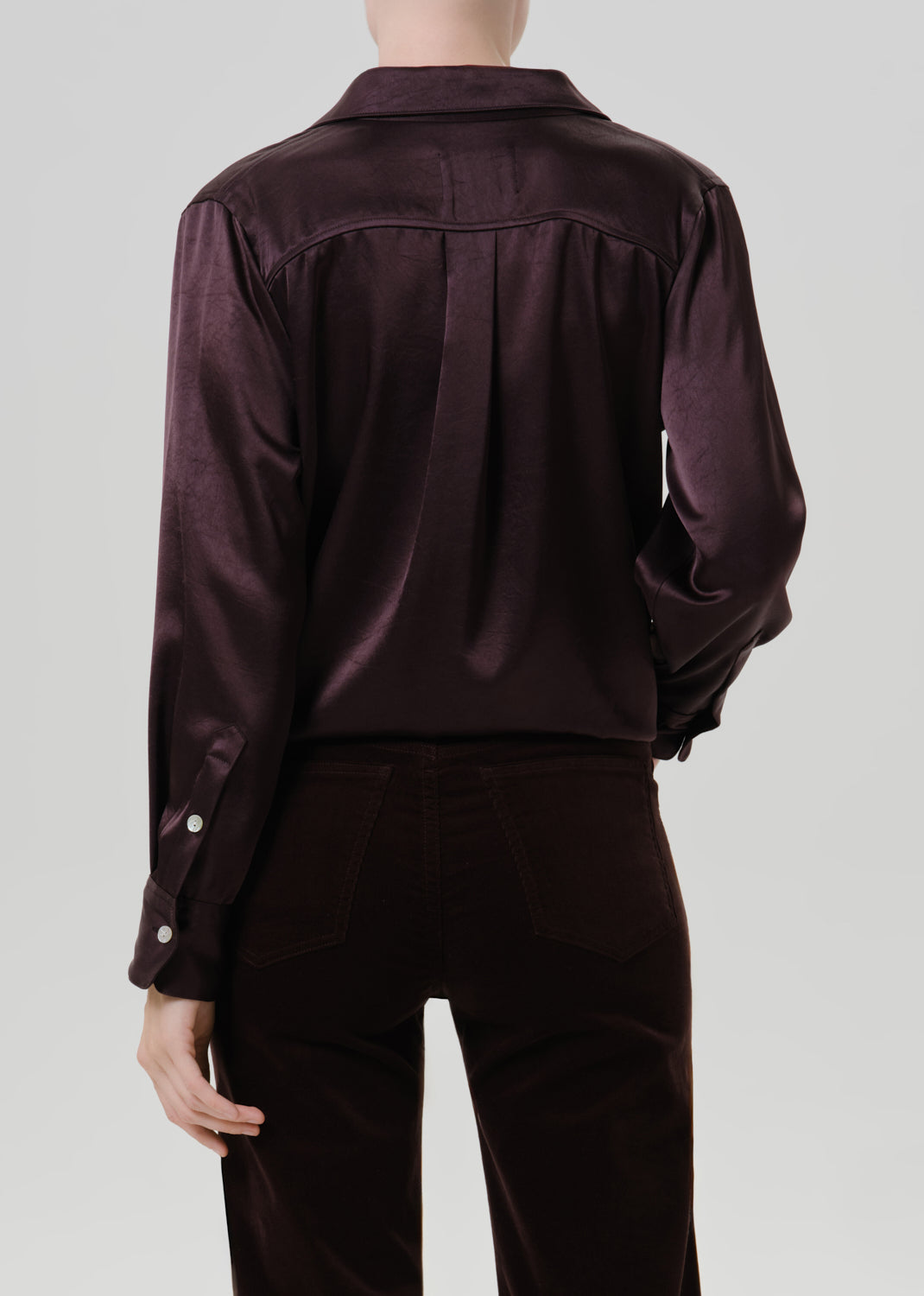Person wearing a dark brown satin button front blouse with dark brown straight leg pants viewed from the back on a grey background