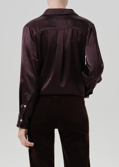 Person wearing a dark brown satin button front blouse with dark brown straight leg pants viewed from the back on a grey background