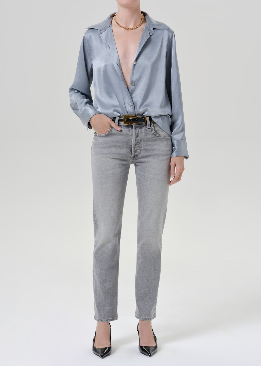 Person wearing a light blue satin button front blouse with light grey straight leg jeans on a grey background