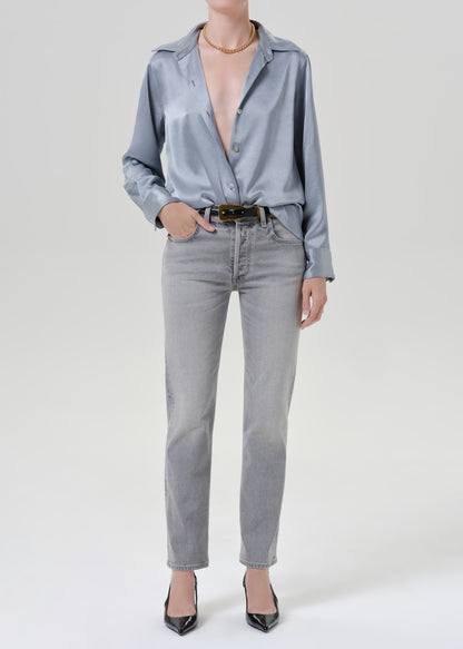 Person wearing a light blue satin button front blouse with light grey straight leg jeans on a grey background