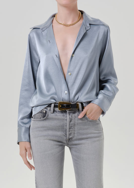 Person wearing a light blue satin button front blouse on a grey background