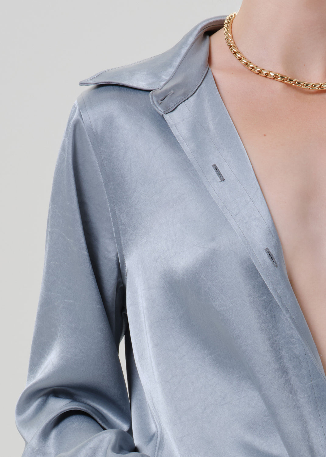 Close-up of a light blue satin button front blouse on a grey background