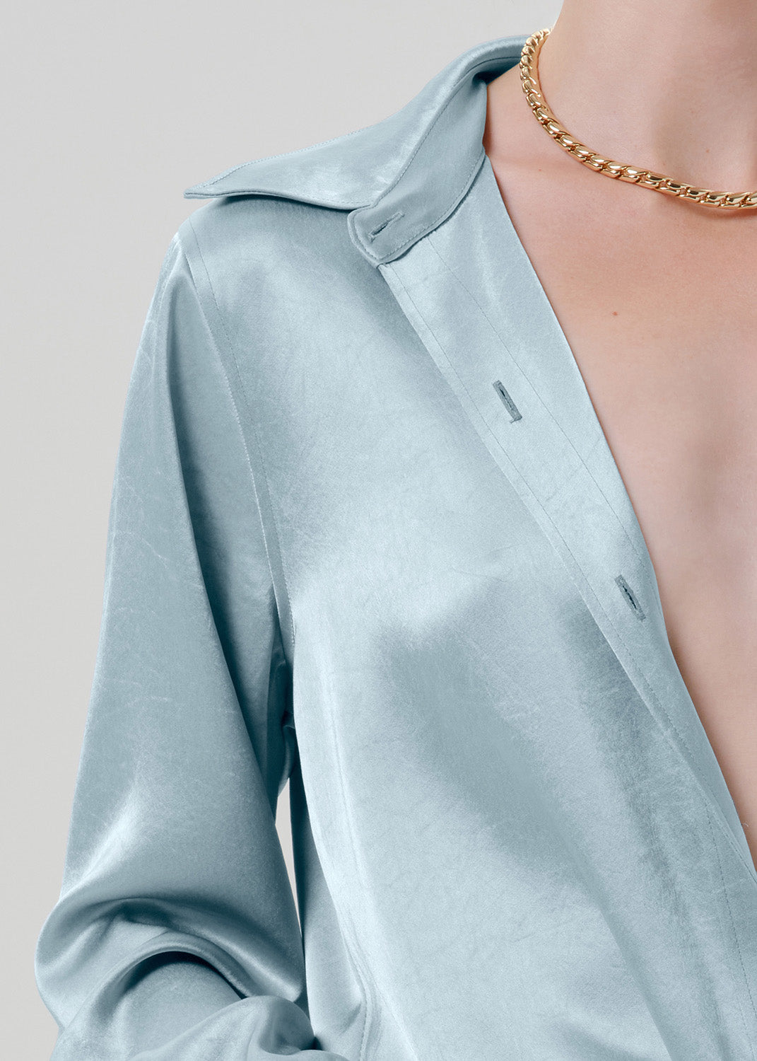 Close-up of a light blue satin button-up shirt on a grey background.