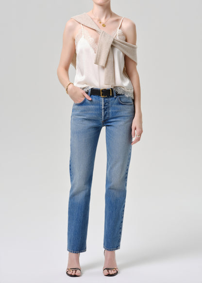 Woman wearing a beige top and blue jeans on a grey background