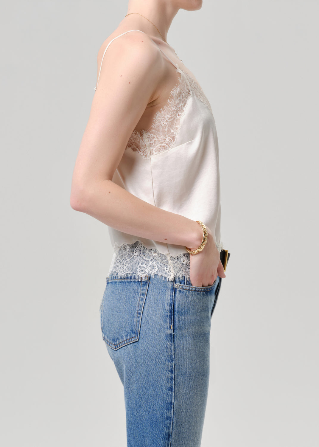 Person wearing a white lace top and blue jeans on a grey background