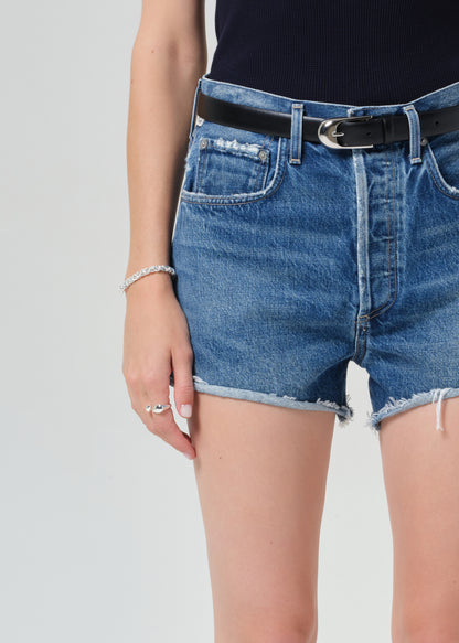 Person wearing a navy t-shirt and denim shorts on a grey background