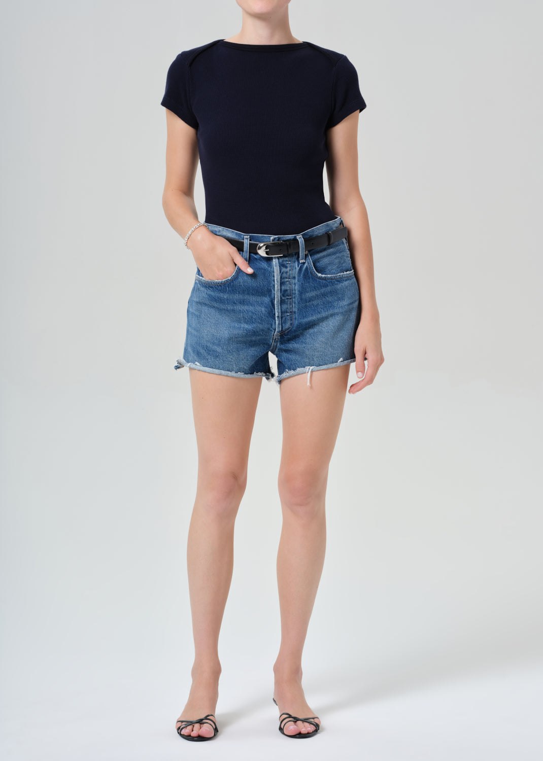 Person wearing a navy t-shirt and denim shorts on a grey background