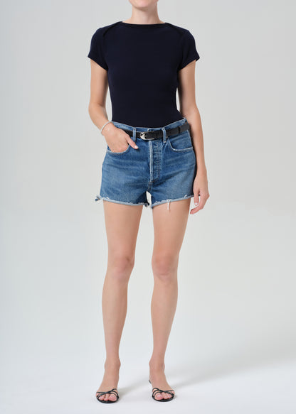 Person wearing a navy t-shirt and denim shorts on a grey background