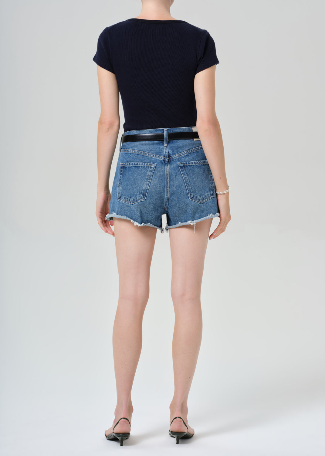 Person wearing a navy t-shirt and denim shorts on a grey background
