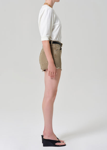 Person wearing a white top and brown shorts on a plain background