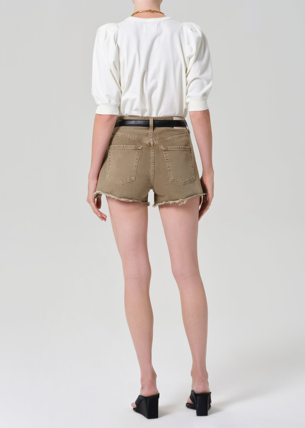 Person wearing a white top and brown shorts on a plain background