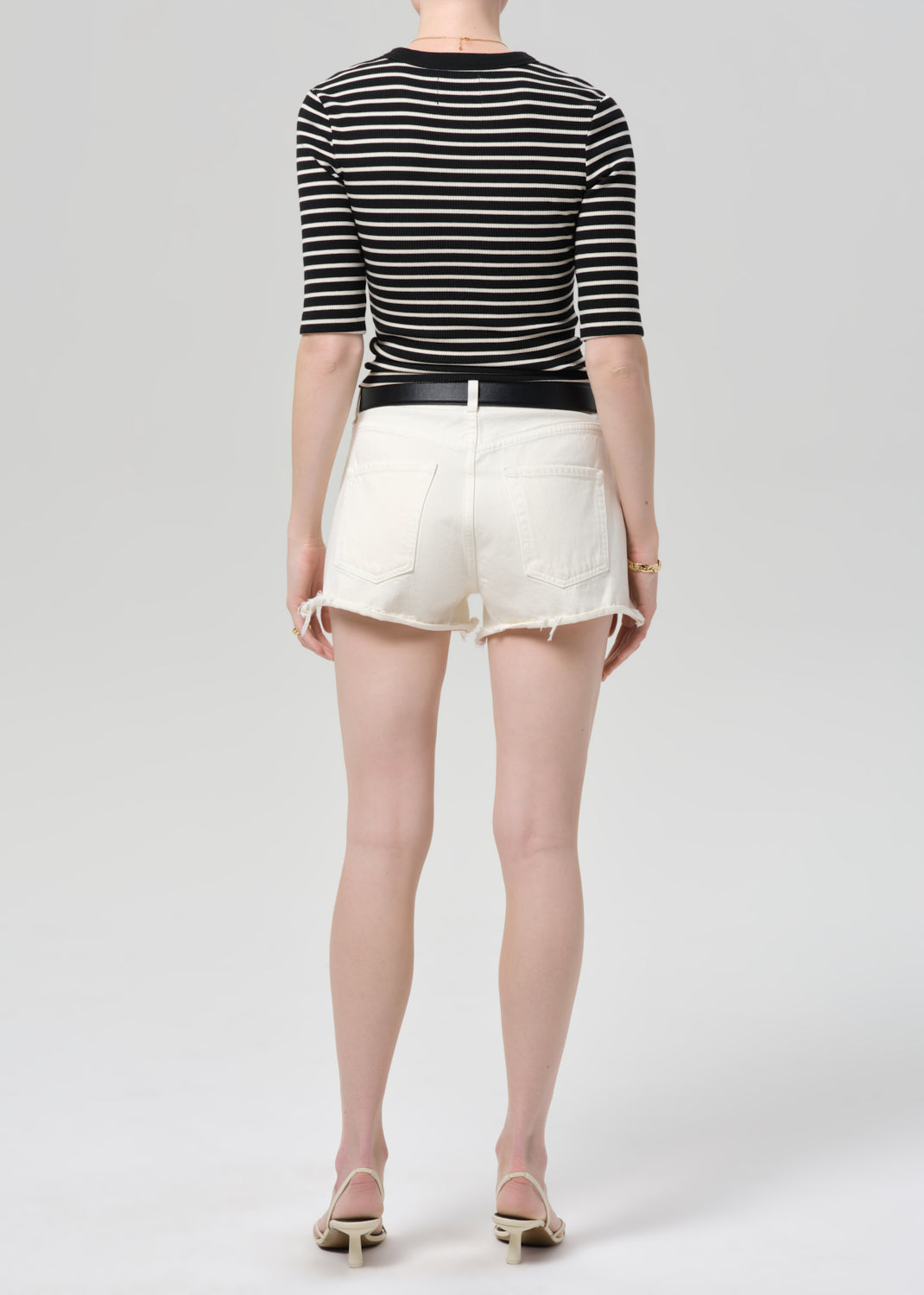 Person wearing a black and white striped shirt with a belt and white shorts on a white background
