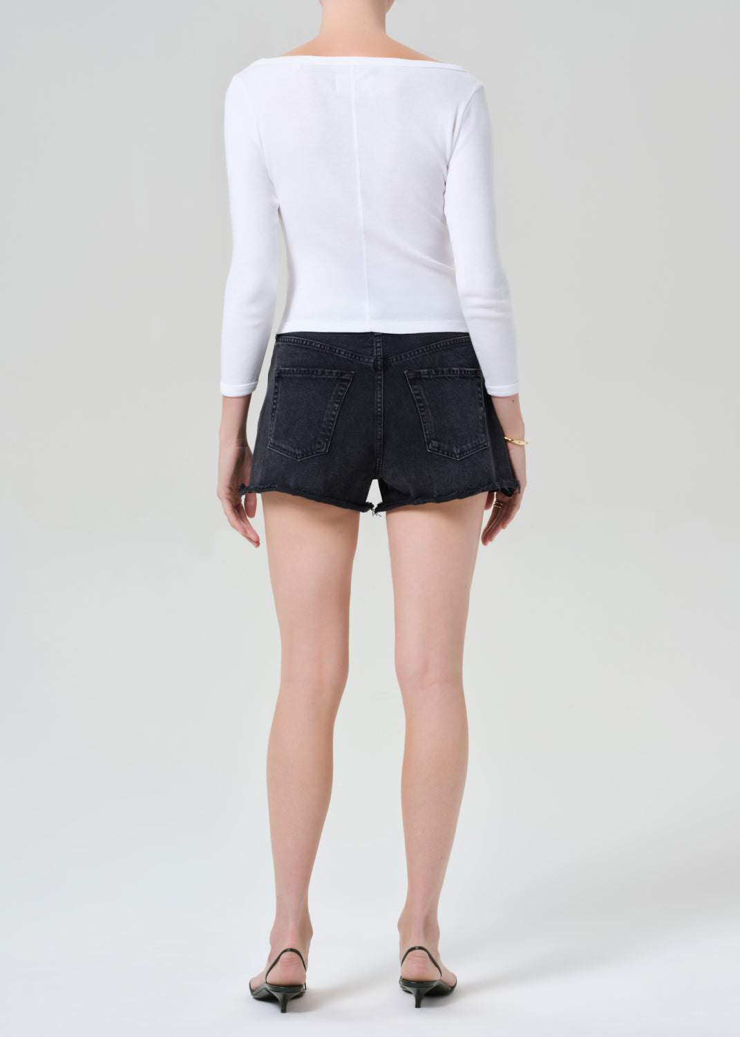 Person wearing a white long-sleeve top and black shorts on a plain background