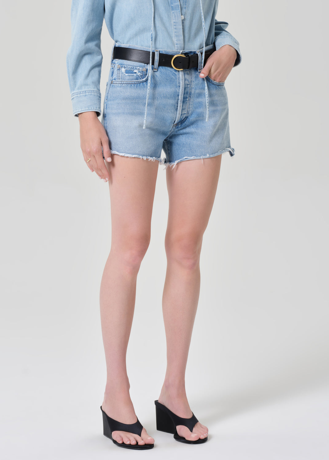 Person wearing a light blue denim shirt with shorts on a grey background