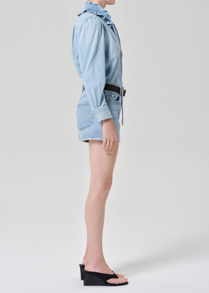 Person wearing a light blue denim shirt with shorts on a grey background