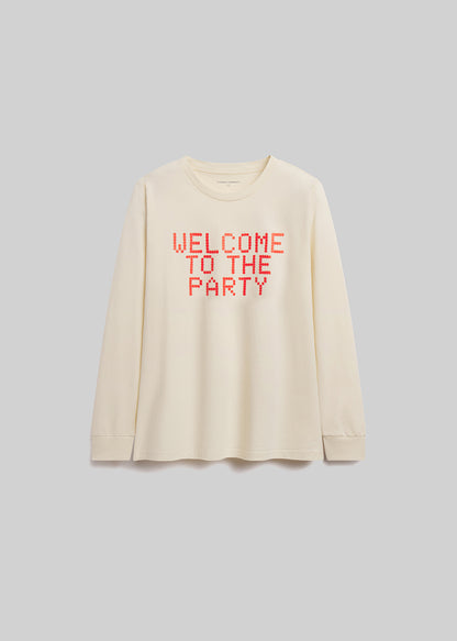 Beige long-sleeve shirt with 'WELCOME TO THE PARTY' text in red on a gray background
