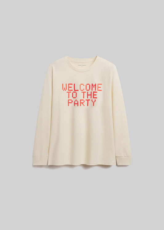 Beige long-sleeve shirt with 'WELCOME TO THE PARTY' text in red on a gray background