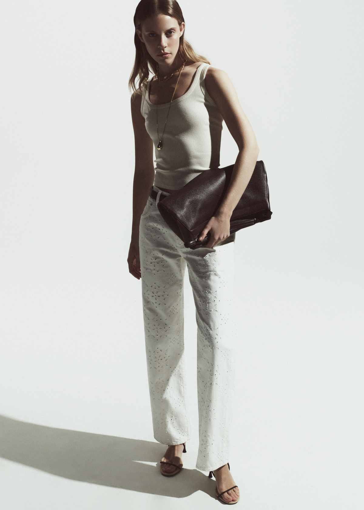 Person wearing white tank top with white jeans with eyelets