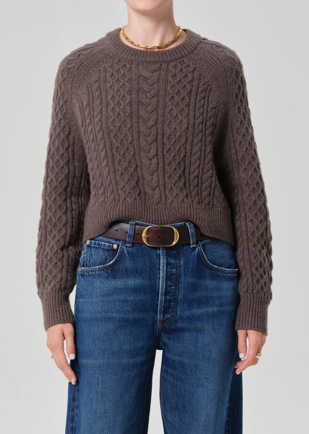 Person wearing a brown cable knit sweater and blue jeans on a plain background