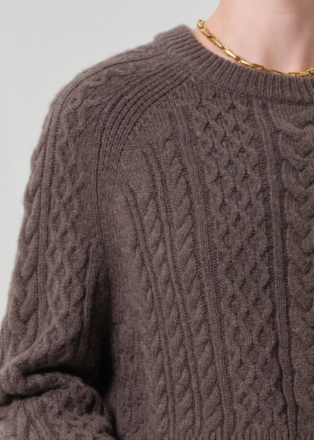 Close-up of a brown cable knit sweater with a plain background