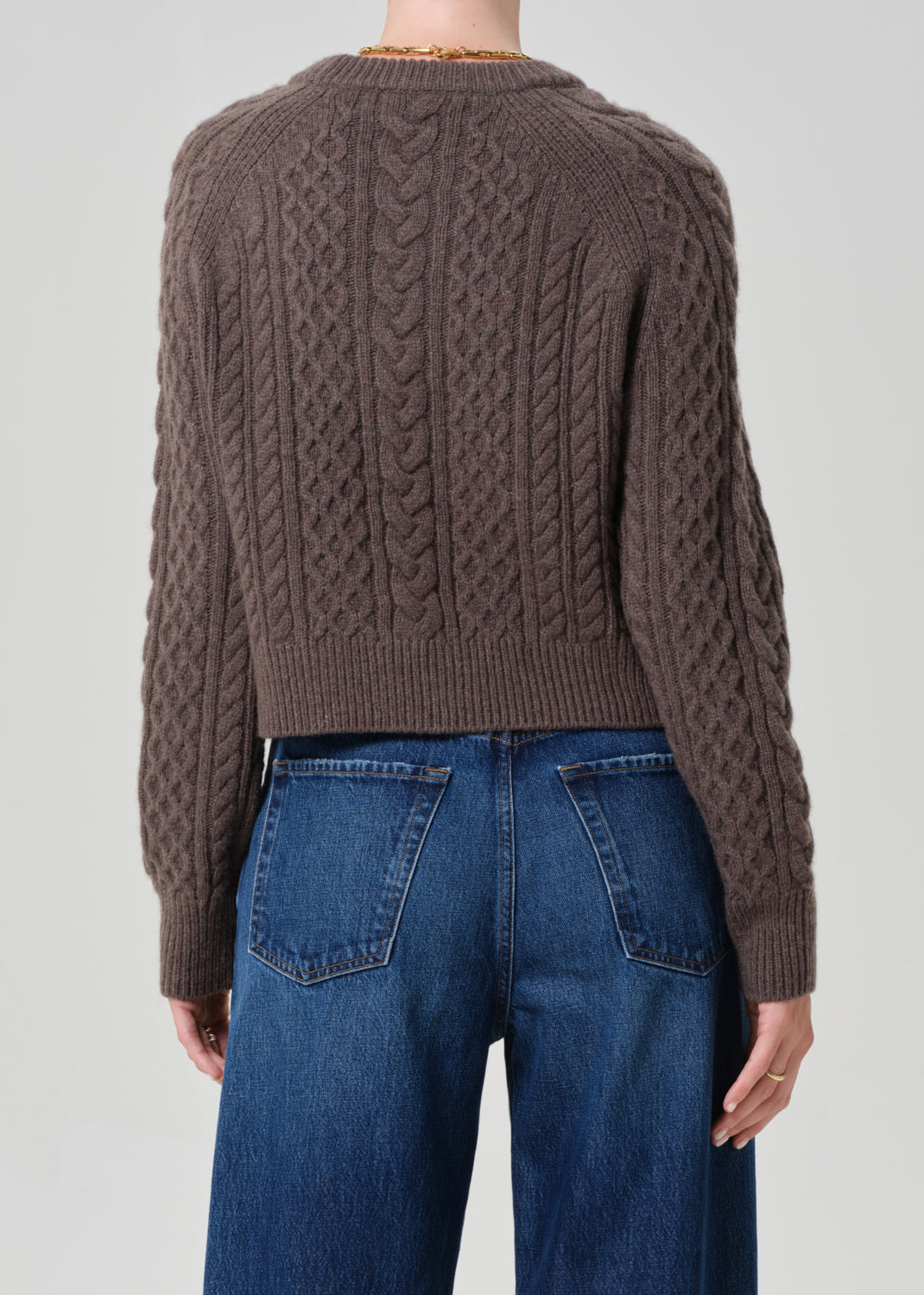Brown cable knit sweater worn by a person on a plain background