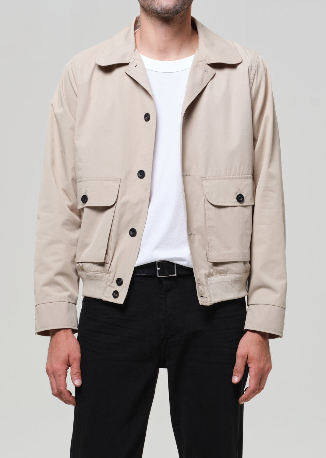 Person wearing a beige jacket with black buttons on a plain background