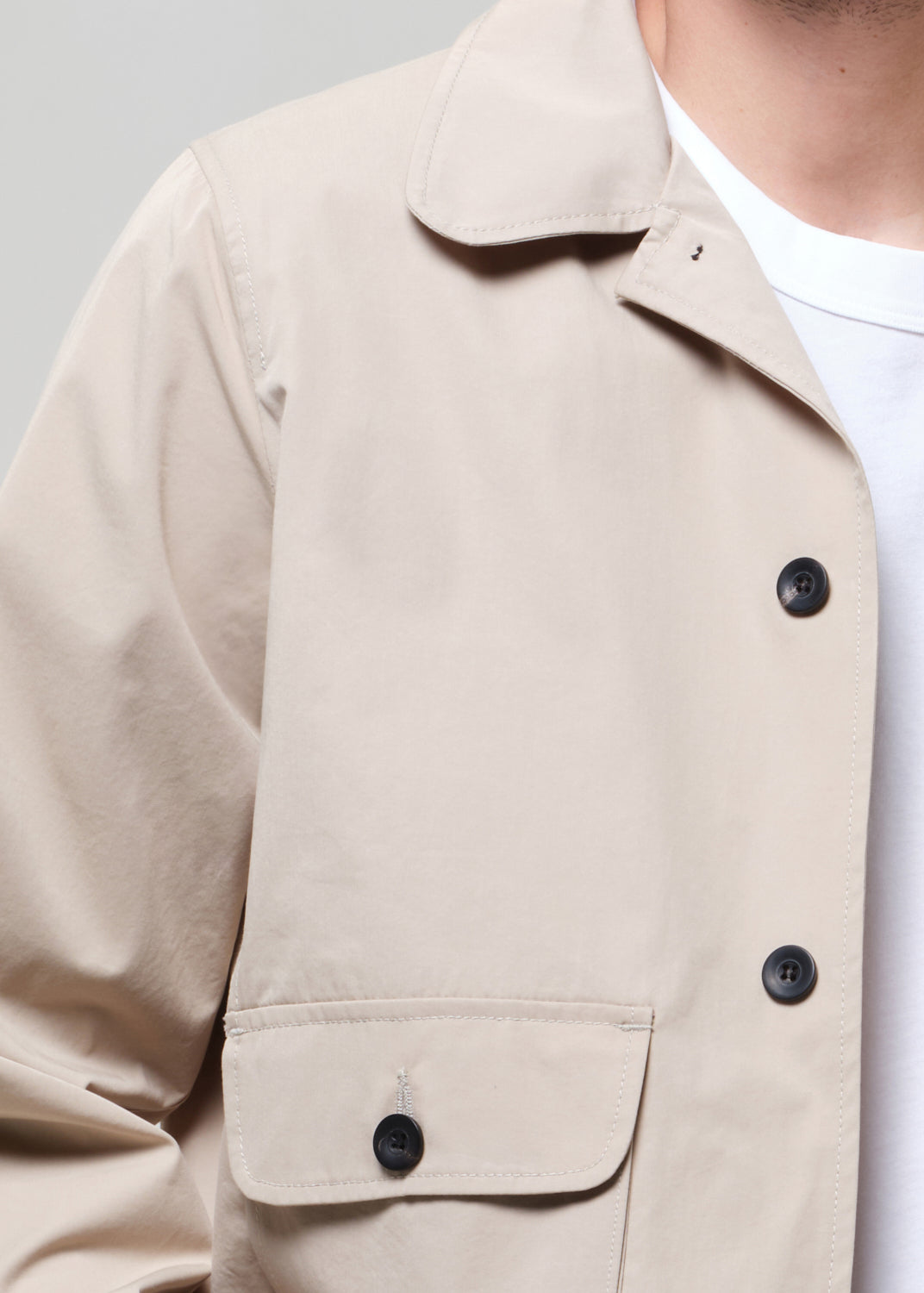 Close-up of a beige jacket with black buttons on a plain background