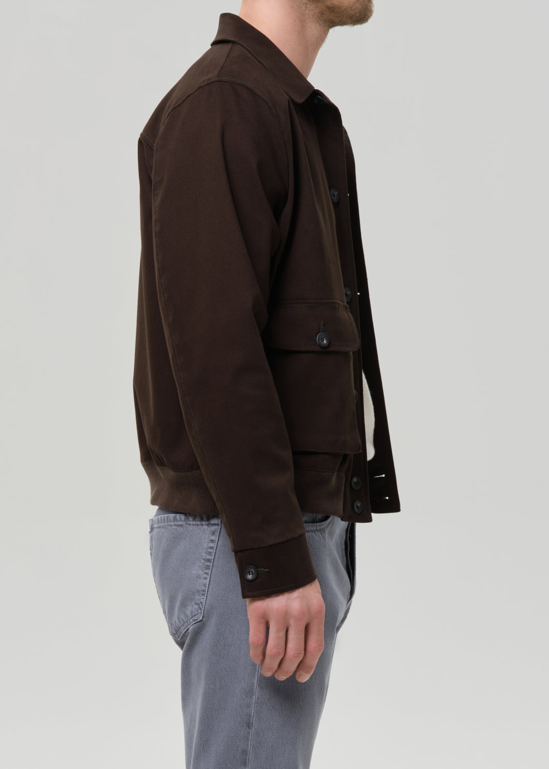 Man wearing a olive jacket and grey pants on a grey background
