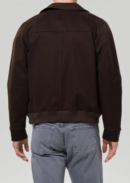 Person wearing a olive jacket and grey pants on a grey background