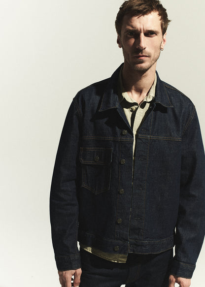 Man wearing a dark denim jacket over a light shirt against a plain background