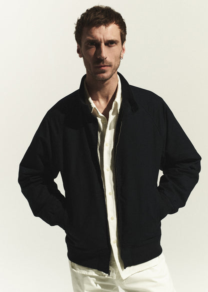 Man wearing a navy jacket over a white shirt on a plain background